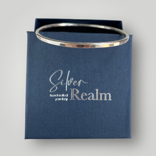 Handmade faceted sterling silver bangle displayed on a Silver Realm Jewellery branded gift box