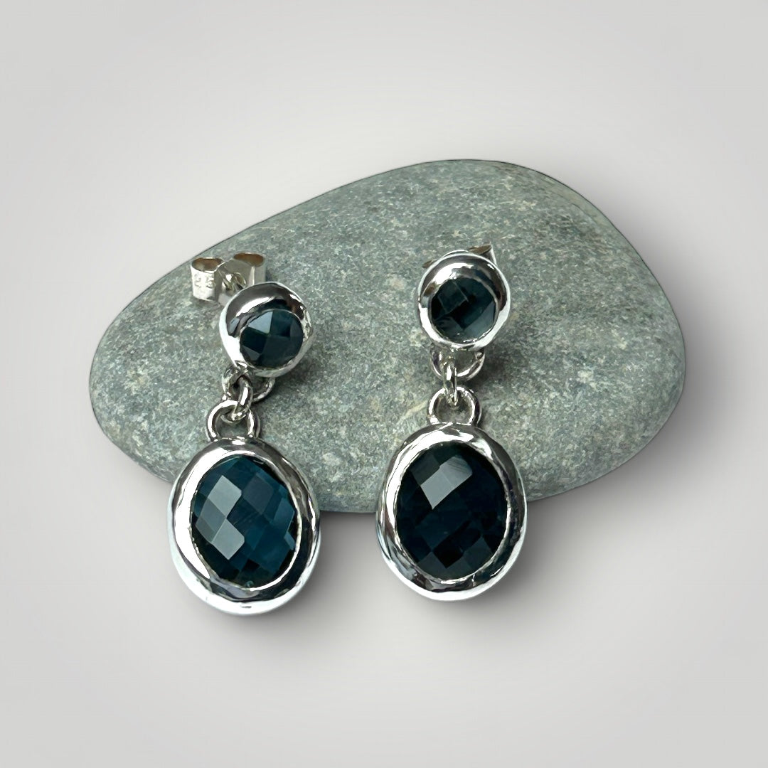 Sterling silver and Blue Topaz earrings displayed on a pebble