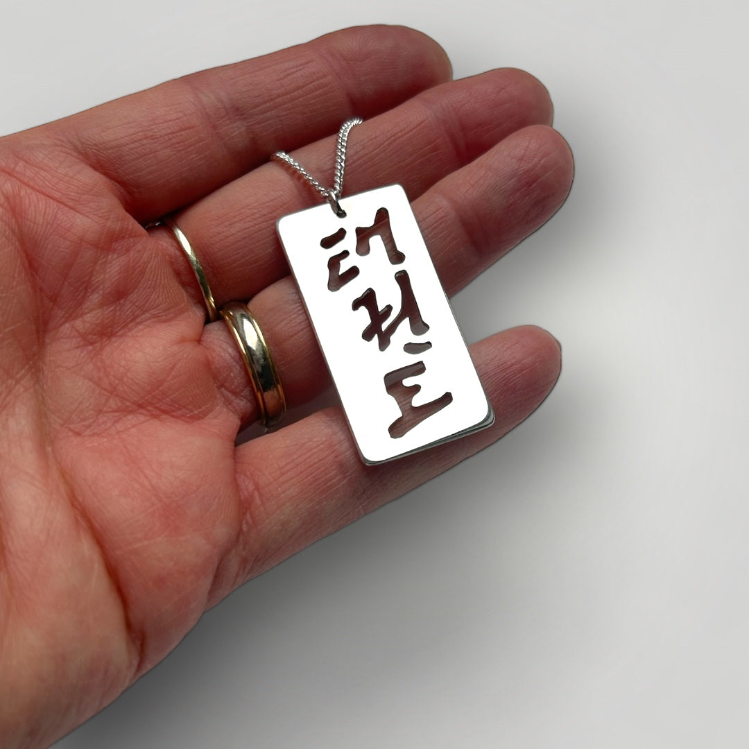 Hand holding a sterling silver pendant with cut-out characters reading Taekwon-Do in Korean script on a gray background