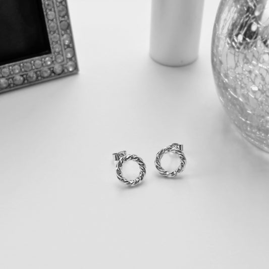 Mini twisted circle sterling silver stud earrings displayed in a monochrome jewellery setting