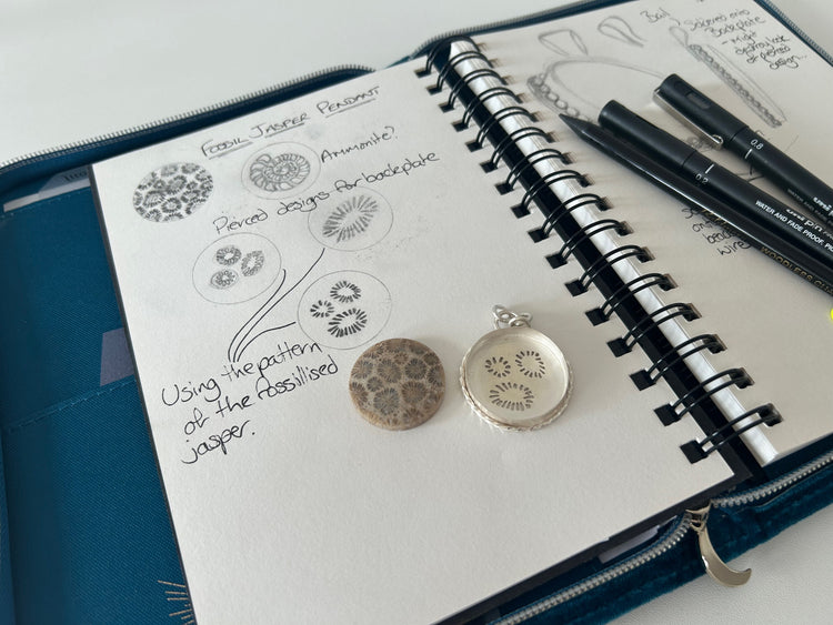Fossil jasper gemstone beside sketches and an unfinished Silver Realm pendant