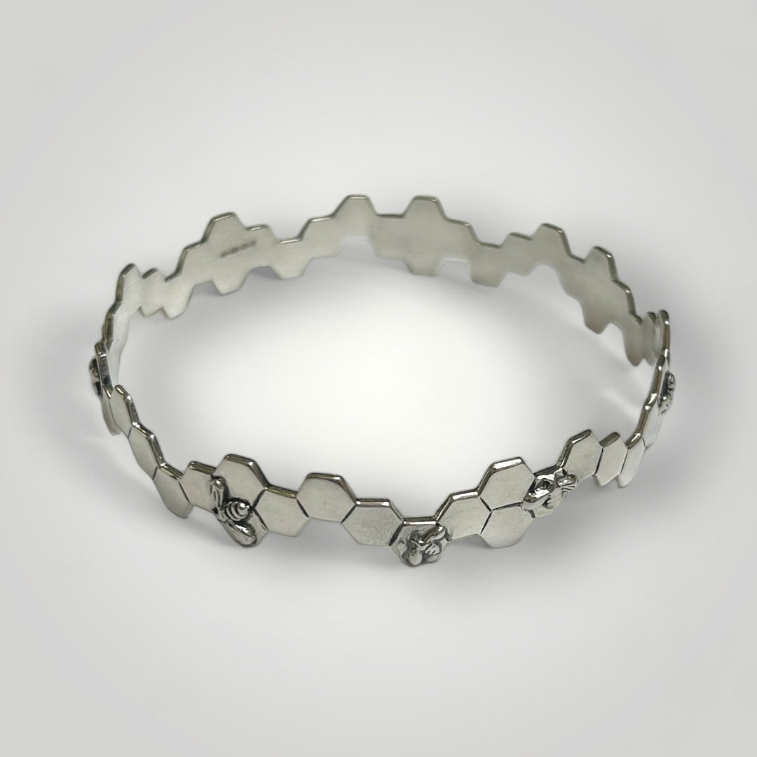 Silver honeycomb and bee bangle on a light grey background