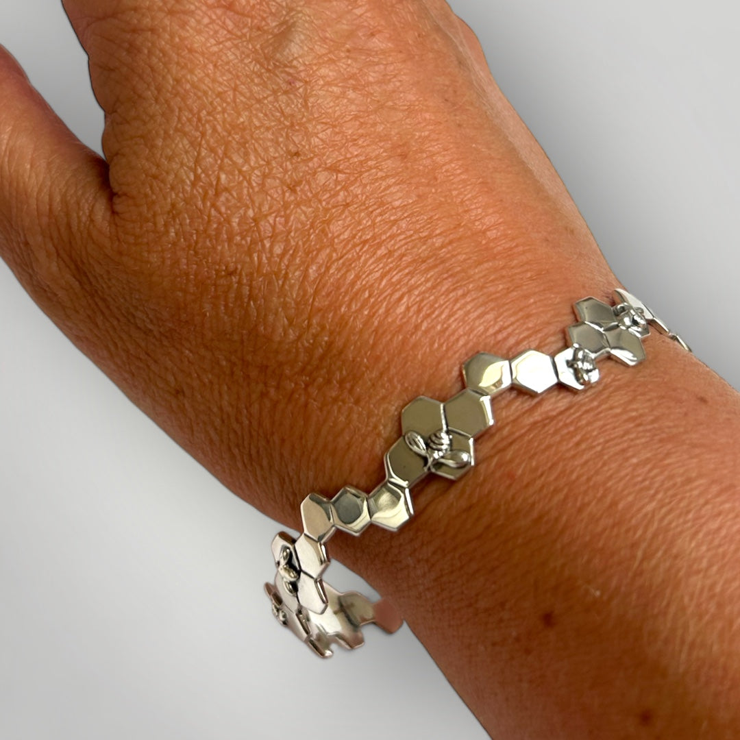 Silver honeycomb and bee bangle on a wrist against a neutral background