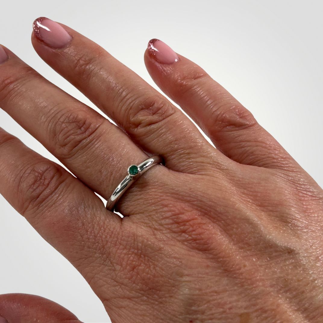 A persons hand wearing a sterling silver and Emerald stacking ring
