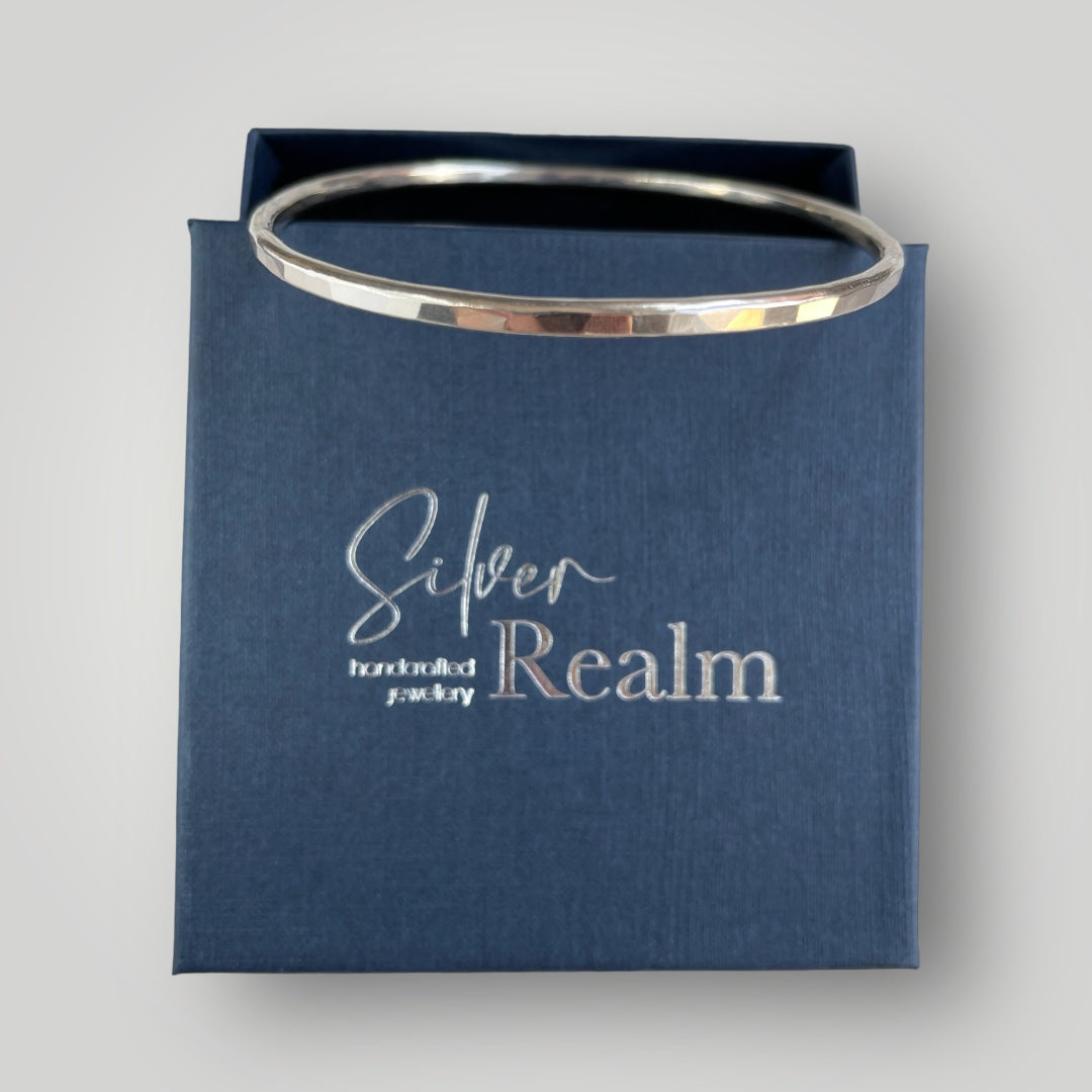 Handmade faceted sterling silver bangle displayed on a Silver Realm Jewellery branded gift box