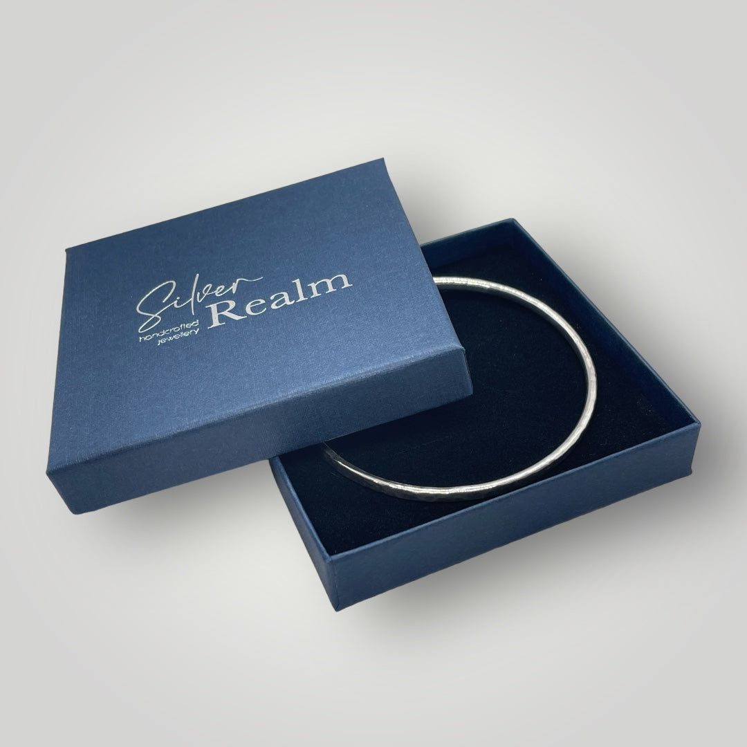 Silver bangle sat in a Silver Realm branded gift box with the lid half on.