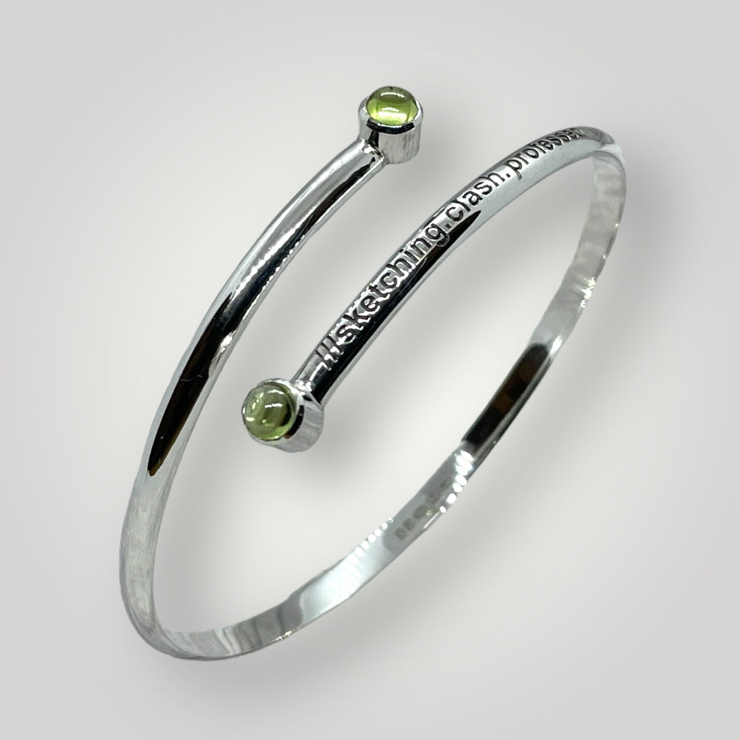 Handmade sterling silver D-profile bangle engraved with a personalised What3Words address and set with two green peridot cabochon gemstones
