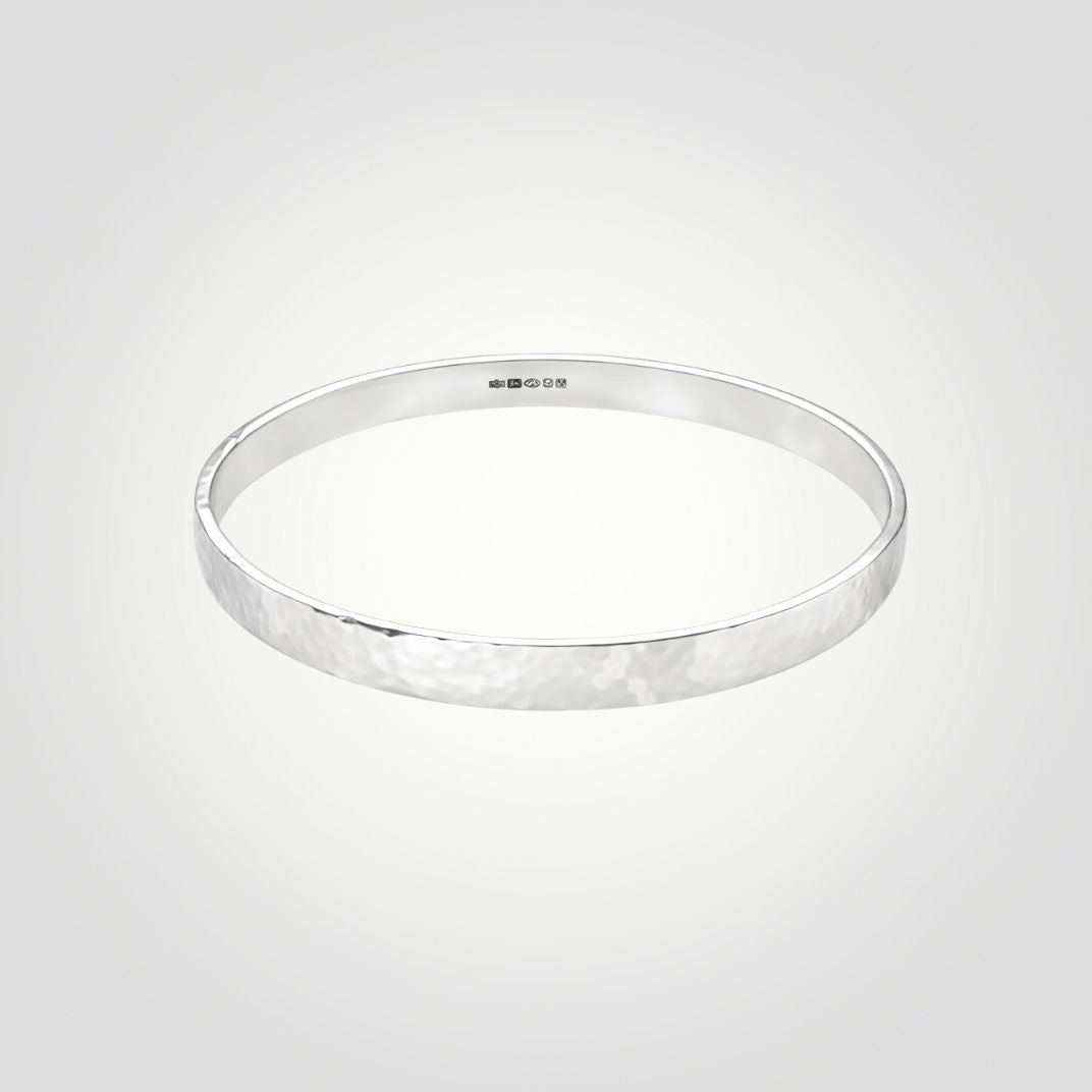Handmade hammered sterling silver bangle with a softly textured finish on a neutral background