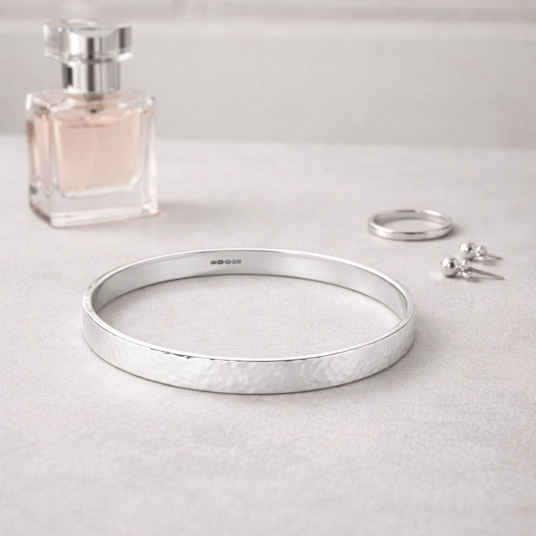 Handmade hammered sterling silver bangle styled on a light grey dressing table with silver jewellery and perfume