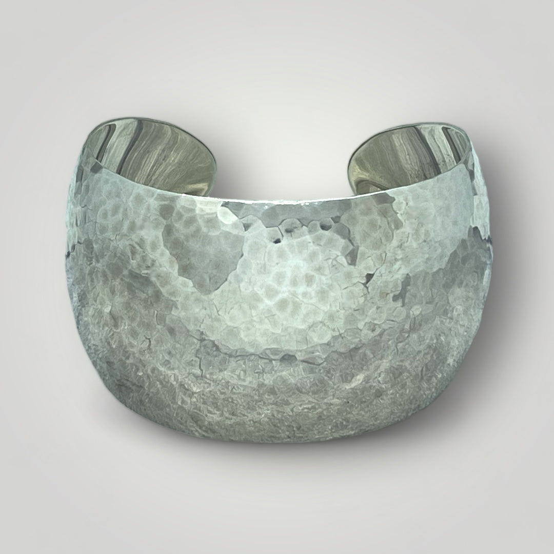 Silver cuff bracelet with a textured surface on a light gray background