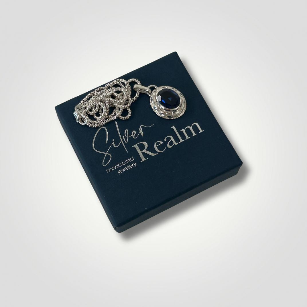 Synthetic sapphire silver pendant with textured handmade setting sitting on a Silver Realm gift box