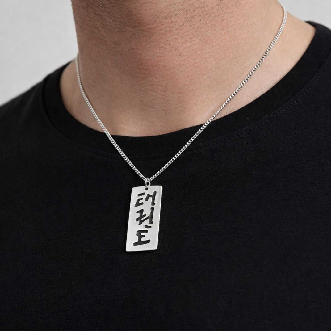 Person wearing a sterling silver pendant with cut-out characters reading Taekwon-Do in Korean script 