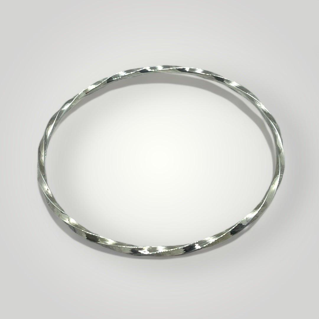 Handmade sterling silver twisted bangle with a polished finish, photographed on a light grey background.