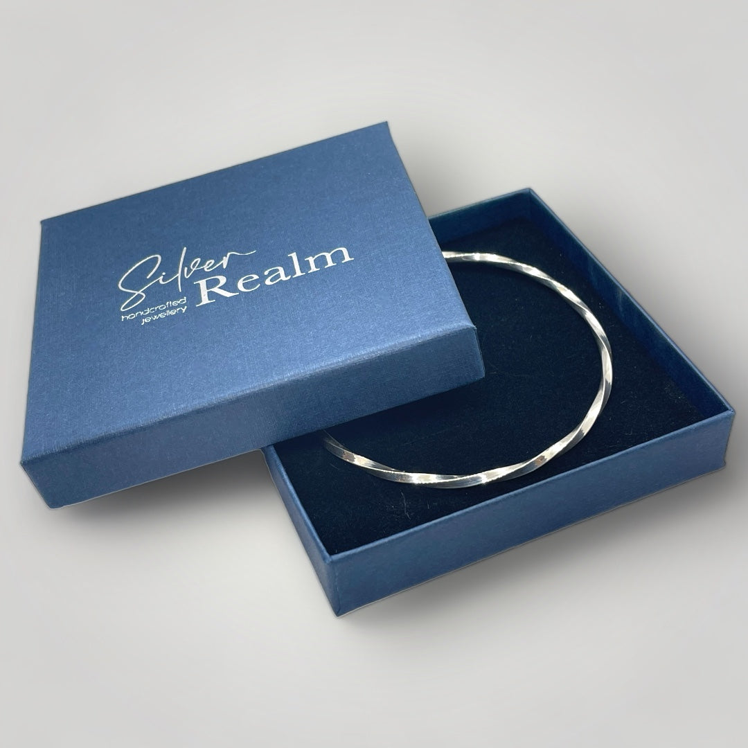Handmade sterling silver twisted bangle presented in a blue Silver Realm branded jewellery gift box.
