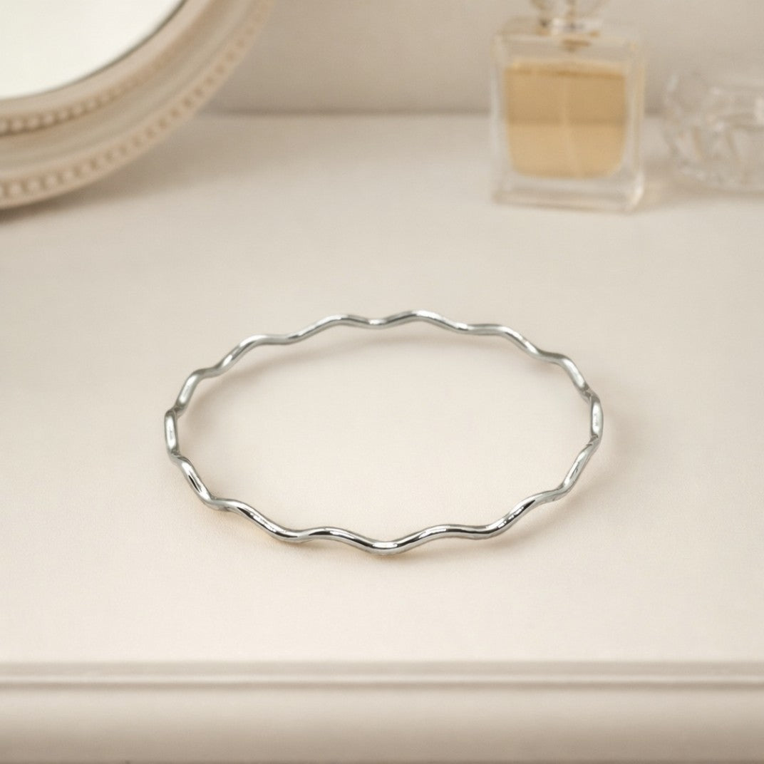 Sterling silver wavy bangle resting on an ivory dressing table, styled with a perfume bottle for a soft, elegant lifestyle jewellery setting.
