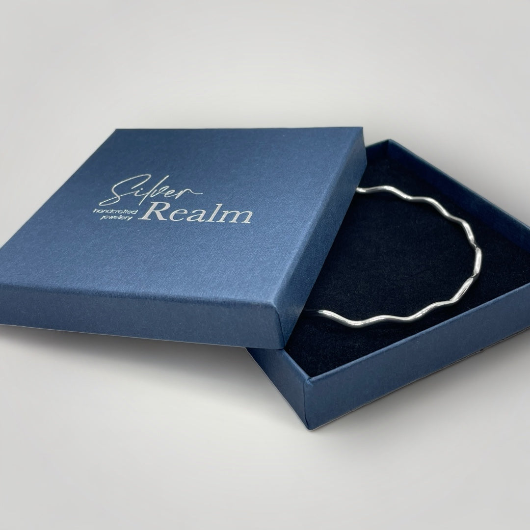 Silver bracelet in an open blue box with 'Silver Realm' branding.