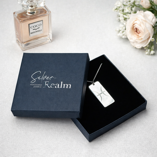Silver necklace tag in an open jewelry box with a bottle of Coco Mademoiselle perfume and flowers on a light surface.