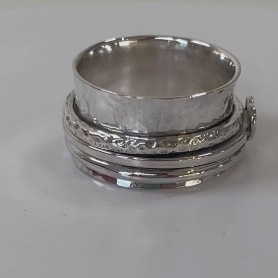 Handmade sterling silver hammered spinner ring with heart detail rotating on a light grey background

