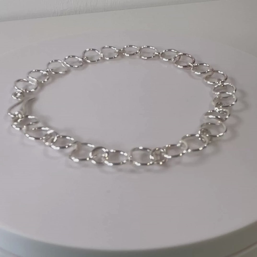 Sterling silver circle link bracelet rotating on a light grey background
