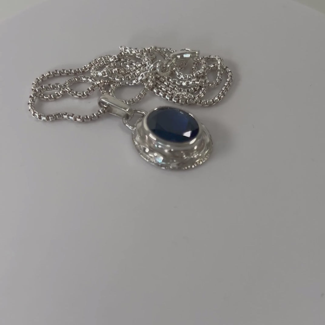 Synthetic sapphire and sterling silver pendant rotating on a light grey background
