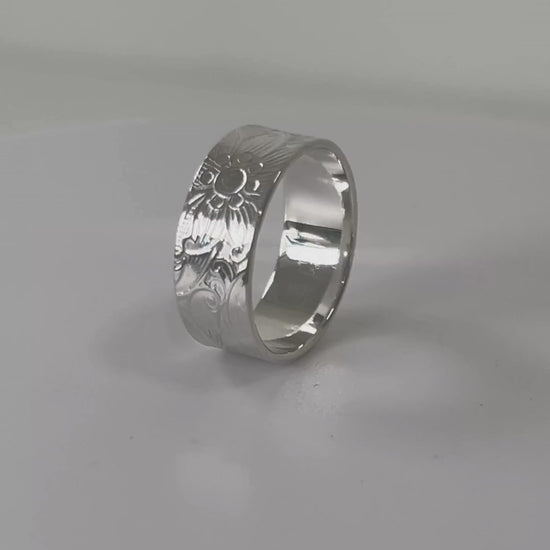 Textured sterling silver wide ring with floral and swirl detail rotating on a light grey background