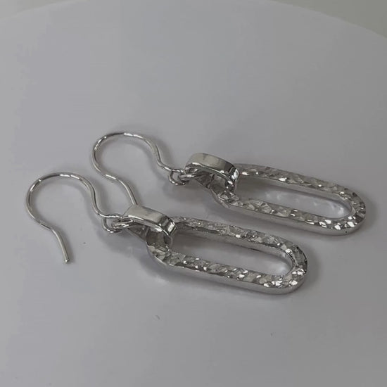 Hammered sterling silver long loop earrings rotating on a light grey background
