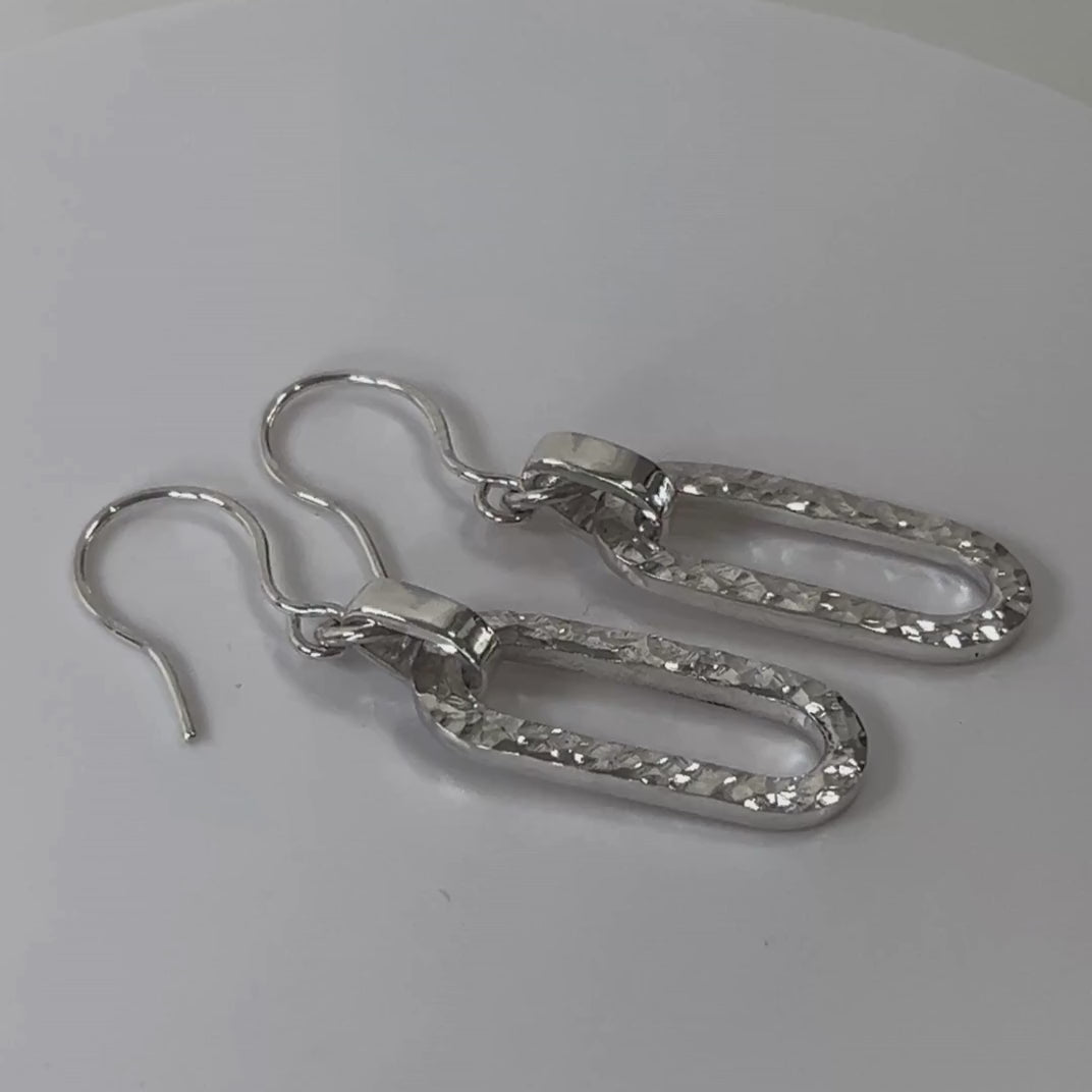 Hammered sterling silver long loop earrings rotating on a light grey background
