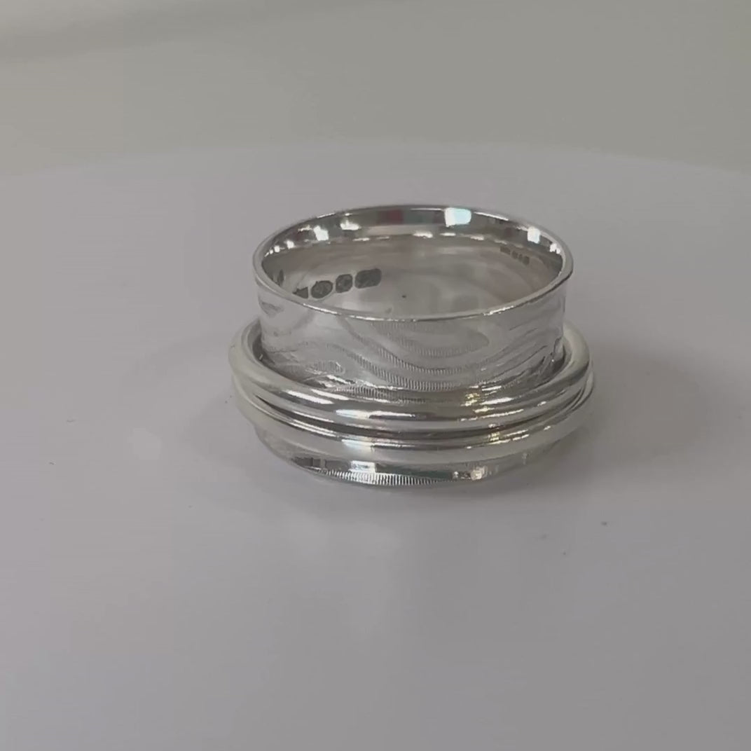 Wide textured sterling silver double spinner ring rotating on a light grey background
