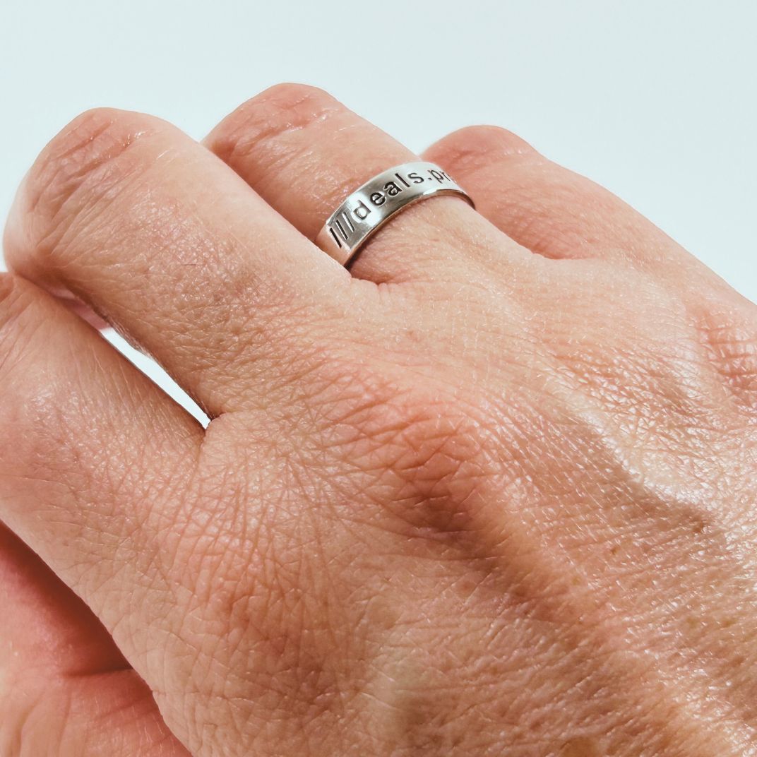 Close-up of a hand wearing a sterling silver what3words ring with engraved text on a light background