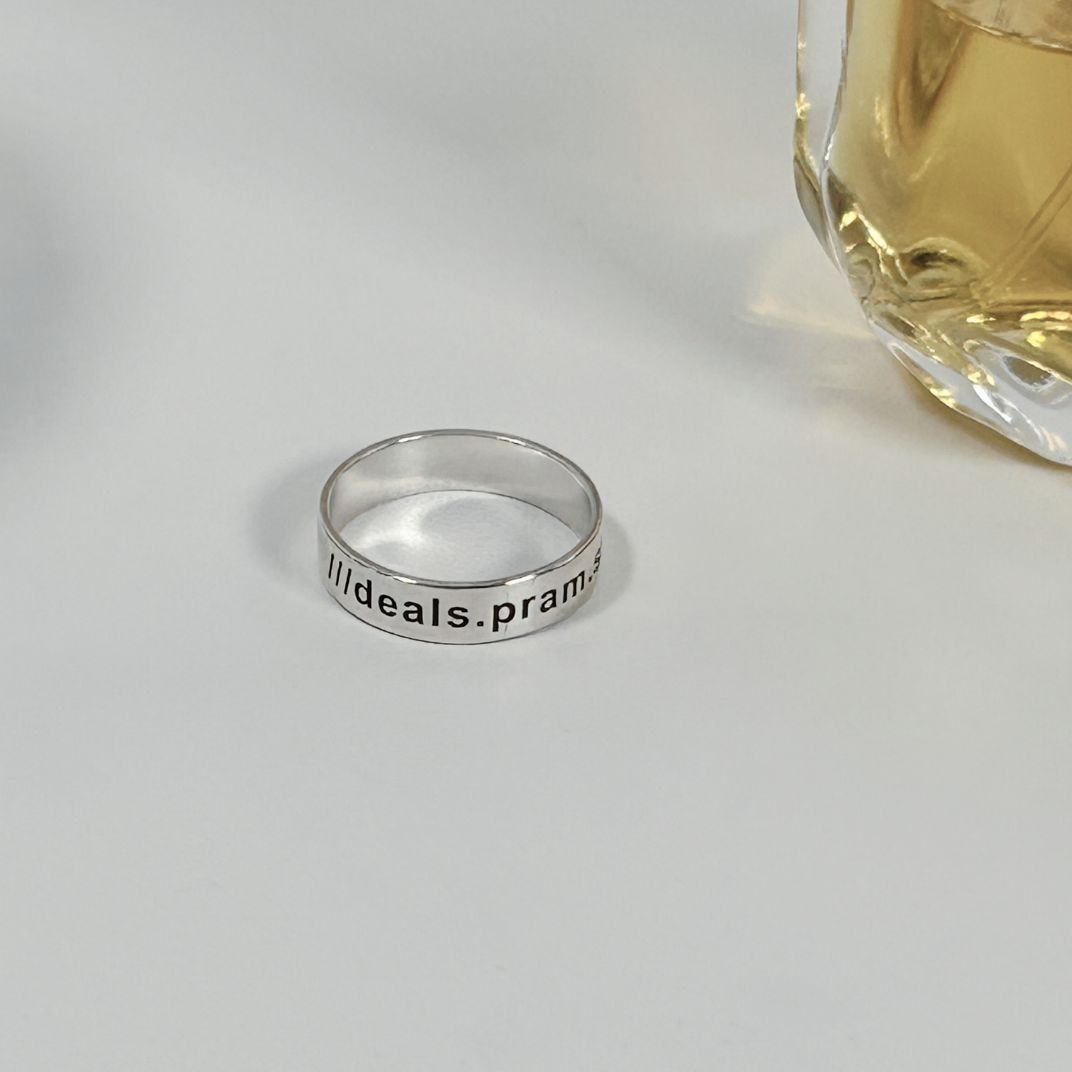 Silver ring with text on a white surface next to a perfume bottle